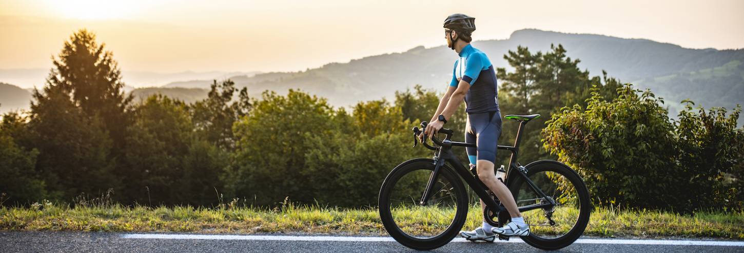 man on road bike stopping on top of hill to take in the view