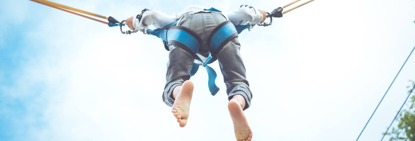 little kid in bungee jumping harness with view from underneathe and bright blue sky