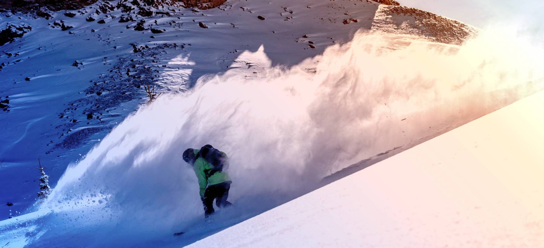 snowboarder kicking up big powder on a downhill run at Copper Mountain Resort during golden hour
