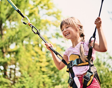 girl bungee jumping with bright green trees in background